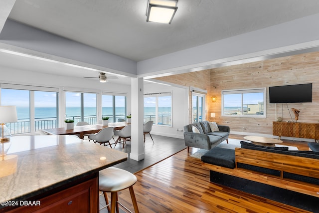 living room with dark wood-type flooring, wooden walls, plenty of natural light, and a water view