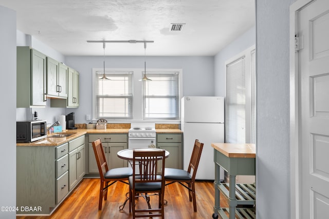 kitchen featuring green cabinets, hanging light fixtures, sink, hardwood / wood-style flooring, and white appliances