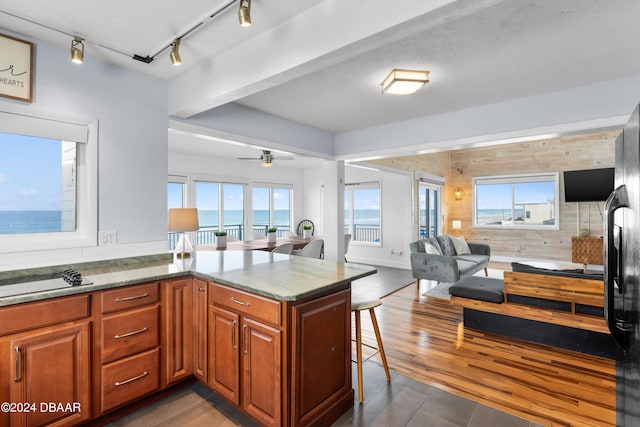 kitchen featuring a kitchen bar, dark wood-type flooring, kitchen peninsula, wooden walls, and ceiling fan