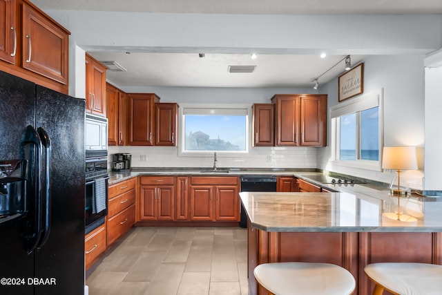 kitchen with a kitchen bar, kitchen peninsula, black appliances, and a healthy amount of sunlight