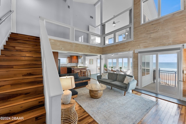 living room featuring ceiling fan, a high ceiling, wood-type flooring, and a water view