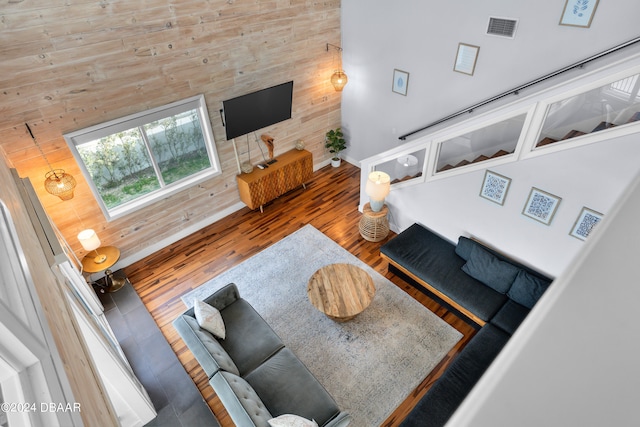 living room with wood-type flooring, wooden walls, and a high ceiling