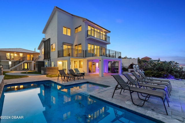 back house at dusk featuring a patio area and a balcony