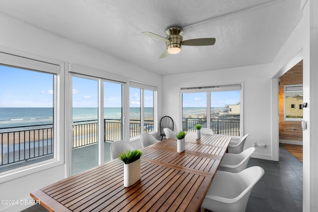 tiled dining room featuring ceiling fan, a view of the beach, a water view, and a textured ceiling