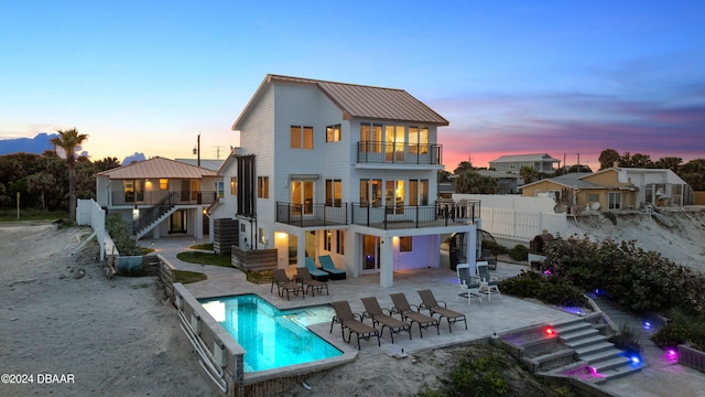 back house at dusk featuring a patio area and a balcony