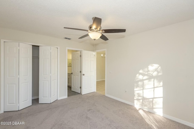 unfurnished bedroom with a textured ceiling, light colored carpet, a closet, and ceiling fan