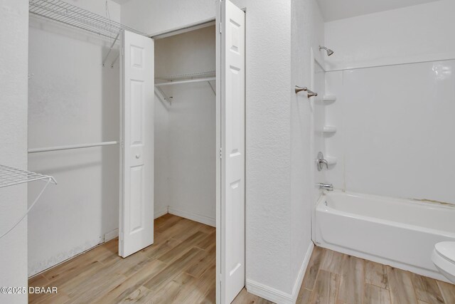 bathroom featuring toilet, tub / shower combination, baseboards, and wood finished floors