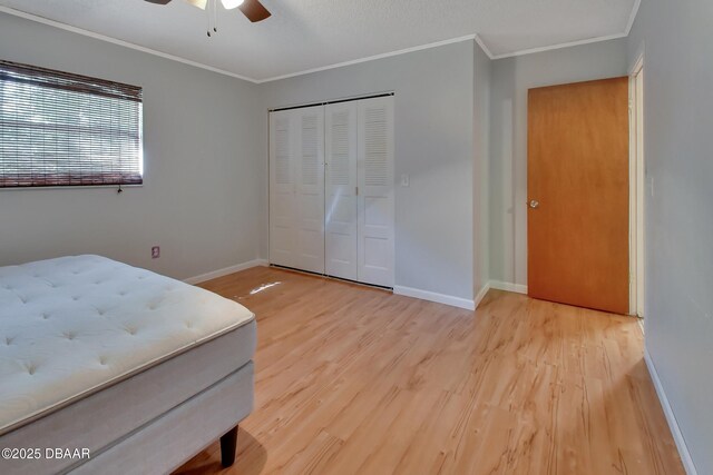 bedroom featuring a closet, baseboards, ornamental molding, wood finished floors, and ceiling fan