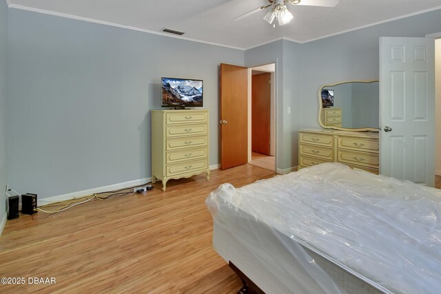 bedroom with visible vents, light wood finished floors, baseboards, ornamental molding, and a ceiling fan