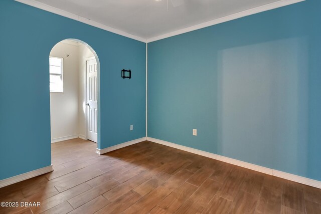 spare room featuring arched walkways, baseboards, and wood finished floors