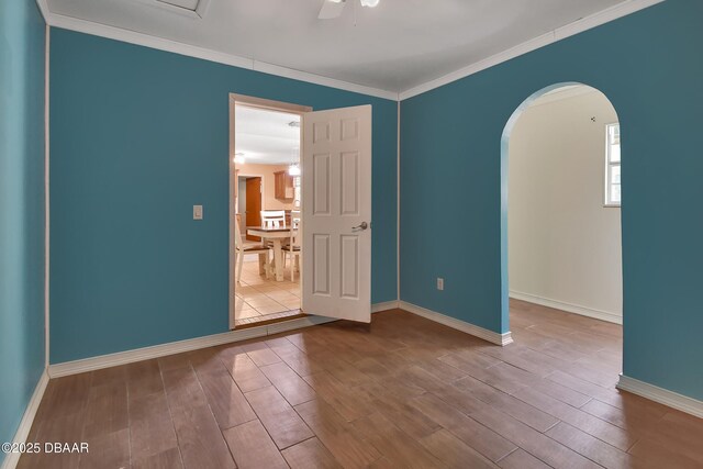 empty room with arched walkways, baseboards, wood finished floors, and crown molding