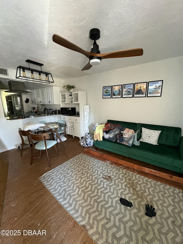 living room with ceiling fan, dark wood-type flooring, and a textured ceiling