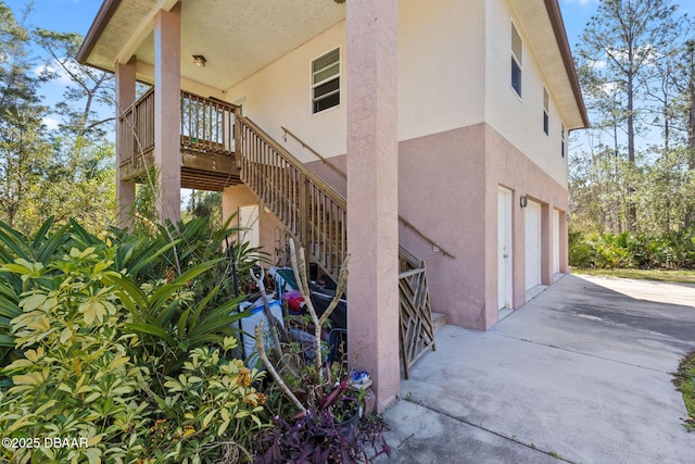 view of side of property featuring stucco siding, a garage, driveway, and stairway