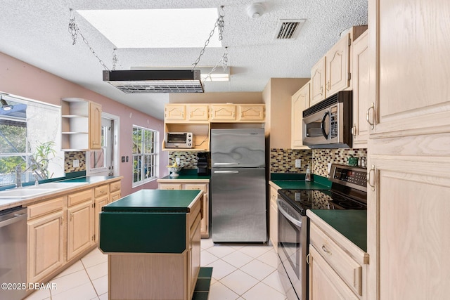 kitchen featuring visible vents, light brown cabinets, a kitchen island, stainless steel appliances, and a sink