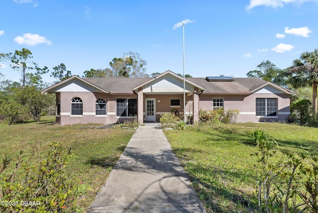 ranch-style house featuring stucco siding, roof mounted solar panels, and a front lawn