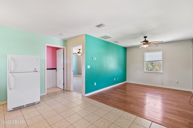 empty room with visible vents, baseboards, ceiling fan, light wood-style floors, and a textured ceiling