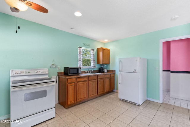 kitchen featuring dark countertops, light tile patterned floors, brown cabinets, white appliances, and a sink