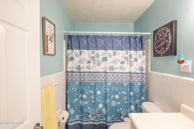 bathroom featuring walk in shower, vanity, toilet, and tile walls