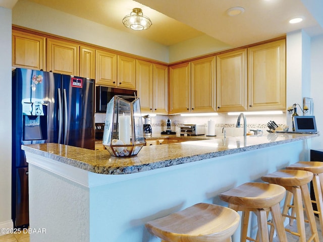 kitchen featuring kitchen peninsula, light stone counters, a breakfast bar area, and fridge with ice dispenser