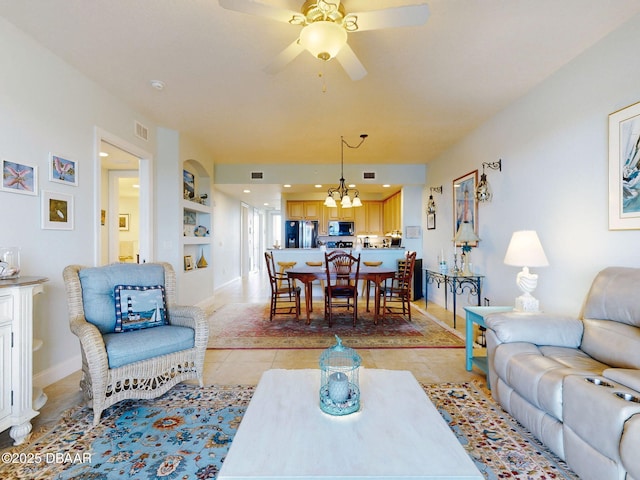 living room featuring built in shelves, light tile patterned floors, and ceiling fan with notable chandelier