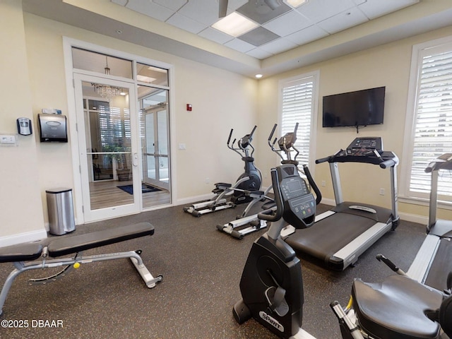 exercise room featuring a raised ceiling, a drop ceiling, and a healthy amount of sunlight