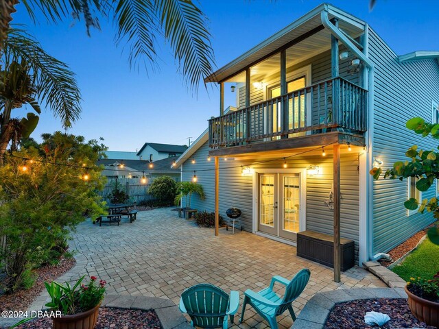 back house at dusk with a balcony, a patio, and french doors