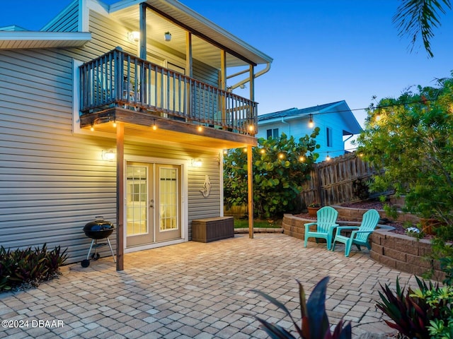 patio terrace at dusk featuring french doors and a balcony