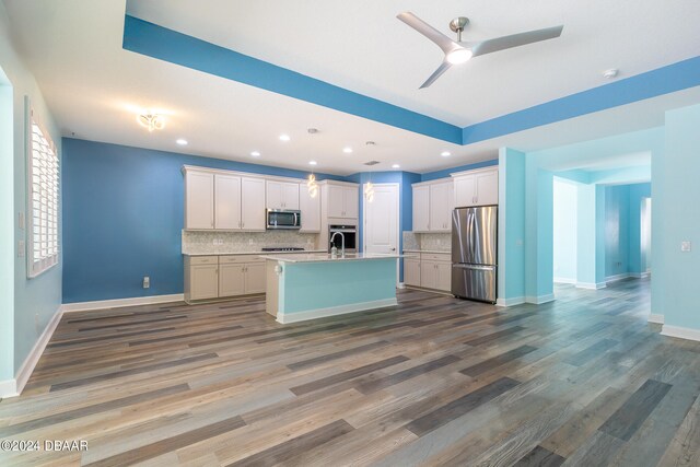 kitchen featuring hardwood / wood-style flooring, an island with sink, backsplash, white cabinetry, and appliances with stainless steel finishes