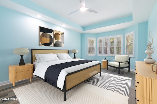 bedroom with hardwood / wood-style floors, ceiling fan, and a raised ceiling