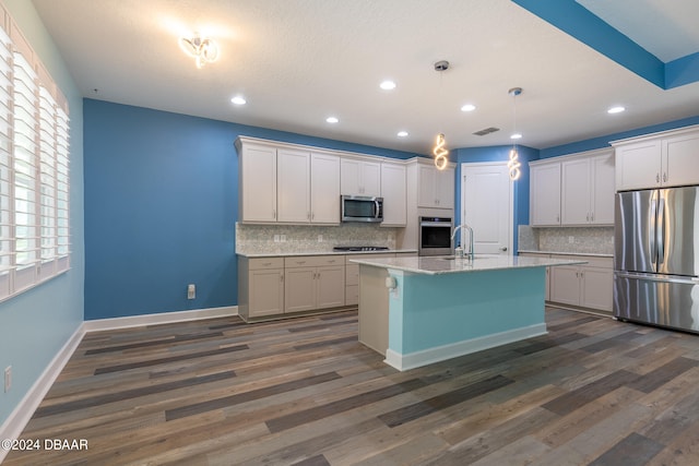 kitchen featuring dark hardwood / wood-style floors, a center island with sink, appliances with stainless steel finishes, and tasteful backsplash