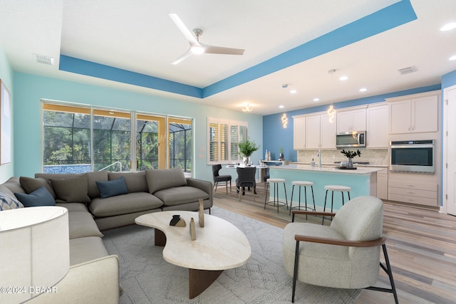 living room with light wood-type flooring, ceiling fan, and a raised ceiling