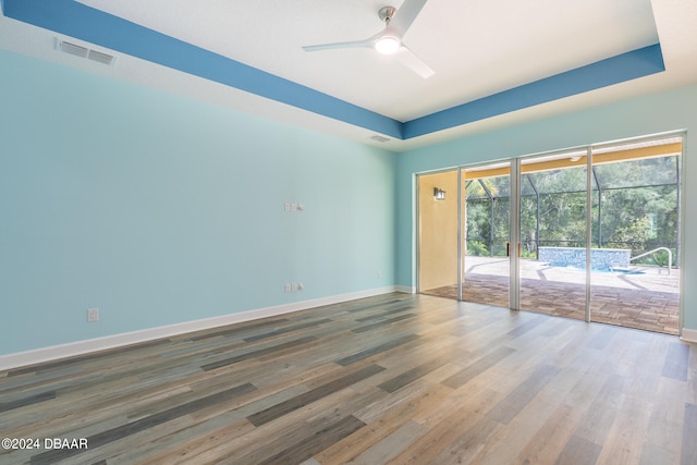 empty room featuring wood-type flooring, ceiling fan, and a tray ceiling