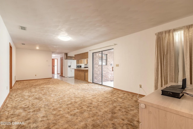 unfurnished living room with visible vents, light carpet, and baseboards