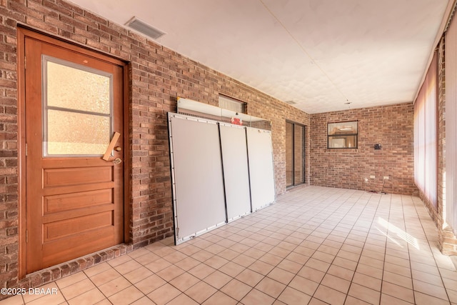 interior space featuring light tile patterned floors, visible vents, and brick wall