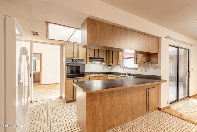 kitchen featuring visible vents, a peninsula, a sink, oven, and dark countertops