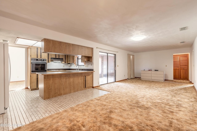 kitchen featuring visible vents, open floor plan, freestanding refrigerator, wall oven, and a peninsula