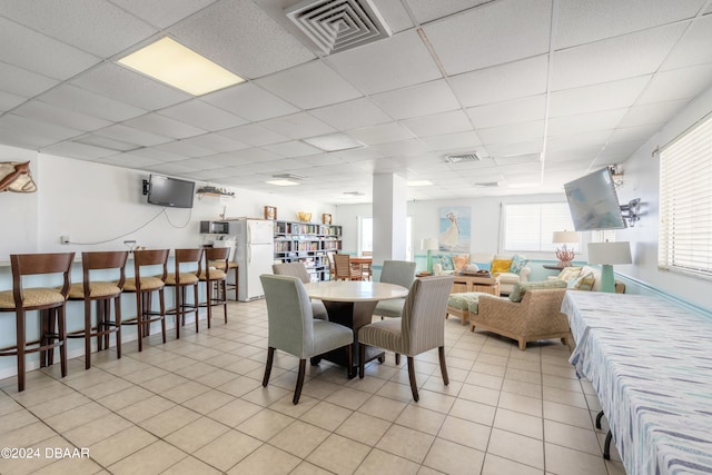 dining area featuring a drop ceiling, light tile patterned floors, and a healthy amount of sunlight