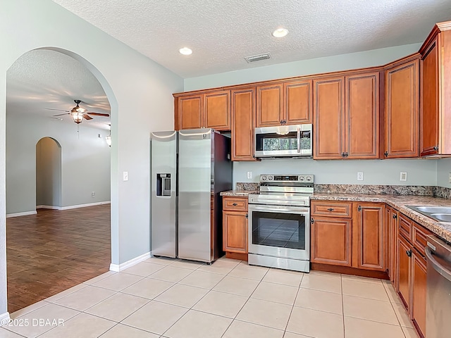 189 Perfect Dr, Daytona Beach, FL 32124 - kitchen featuring appliances with stainless steel finishes, a textured ceiling, arched walkways, ceiling fan, and brown cabinetry