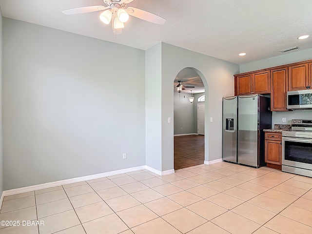 189 Perfect Dr, Daytona Beach, FL 32124 - kitchen featuring appliances with stainless steel finishes, a ceiling fan, arched walkways, light tile patterned floors, and brown cabinets