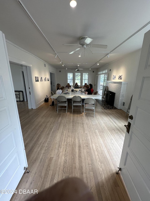 dining space featuring light wood-type flooring, ceiling fan, rail lighting, and a fireplace