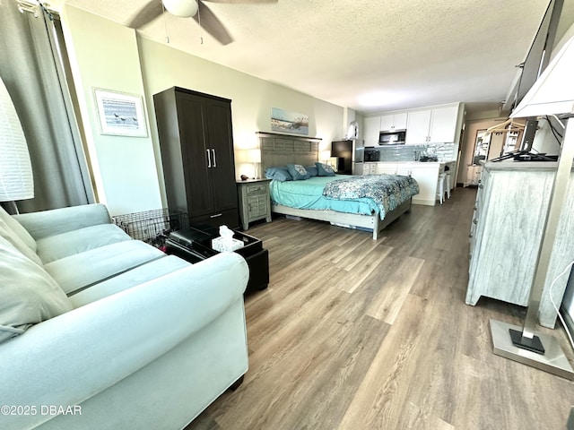 bedroom featuring freestanding refrigerator, wood finished floors, ceiling fan, and a textured ceiling