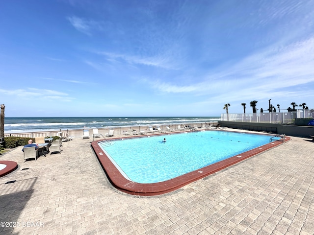 community pool with fence, a water view, and a patio area