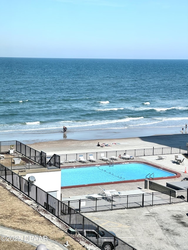 view of pool with a water view, fence, and a view of the beach