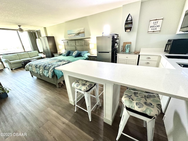 kitchen with dark wood-style floors, open floor plan, a breakfast bar area, and freestanding refrigerator
