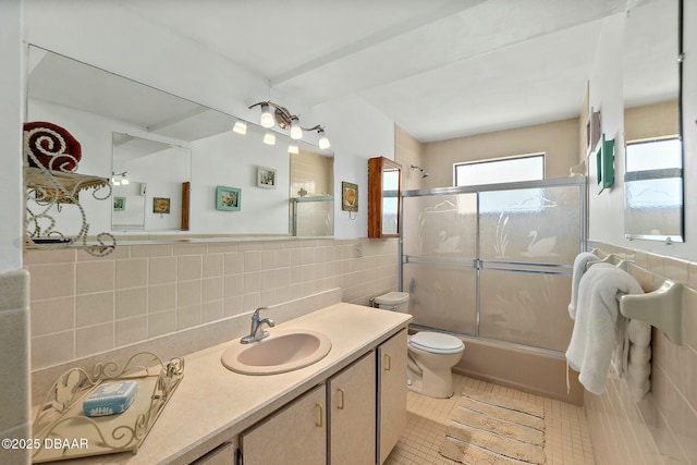 full bath with tile patterned floors, toilet, shower / bath combination with glass door, tile walls, and vanity