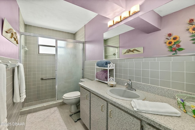 full bath with tile patterned flooring, toilet, vanity, a stall shower, and tile walls