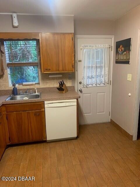 kitchen with light wood finished floors, tasteful backsplash, brown cabinetry, white dishwasher, and a sink