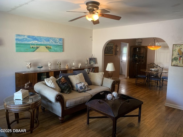 living area with arched walkways, ceiling fan, wood-type flooring, and baseboards