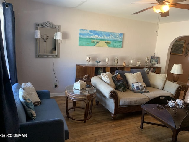 living area featuring a ceiling fan, arched walkways, baseboards, and hardwood / wood-style floors