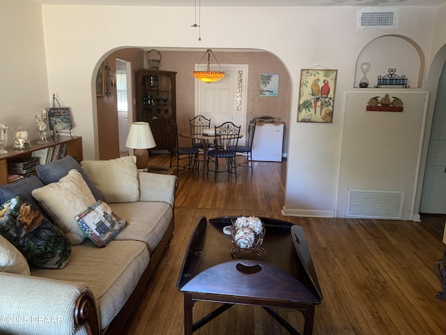 living room with arched walkways, wood-type flooring, and visible vents